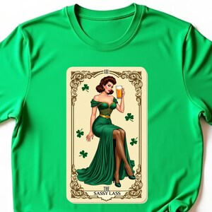May include: Green t-shirt with a vintage-style illustration of a woman in a green dress holding a beer. The illustration is framed with a gold border and has the text "The Sassy Lass" at the bottom.