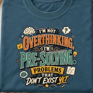 May include: A deep teal t-shirt featuring a graphic print with the text I'M NOT OVERTHINKING, I'M PRE-SOLVING PROBLEMS THAT DON'T EXIST YET. The design includes illustrations of a brain, a lightbulb, a checklist, and a flowchart in orange, yellow, and white.