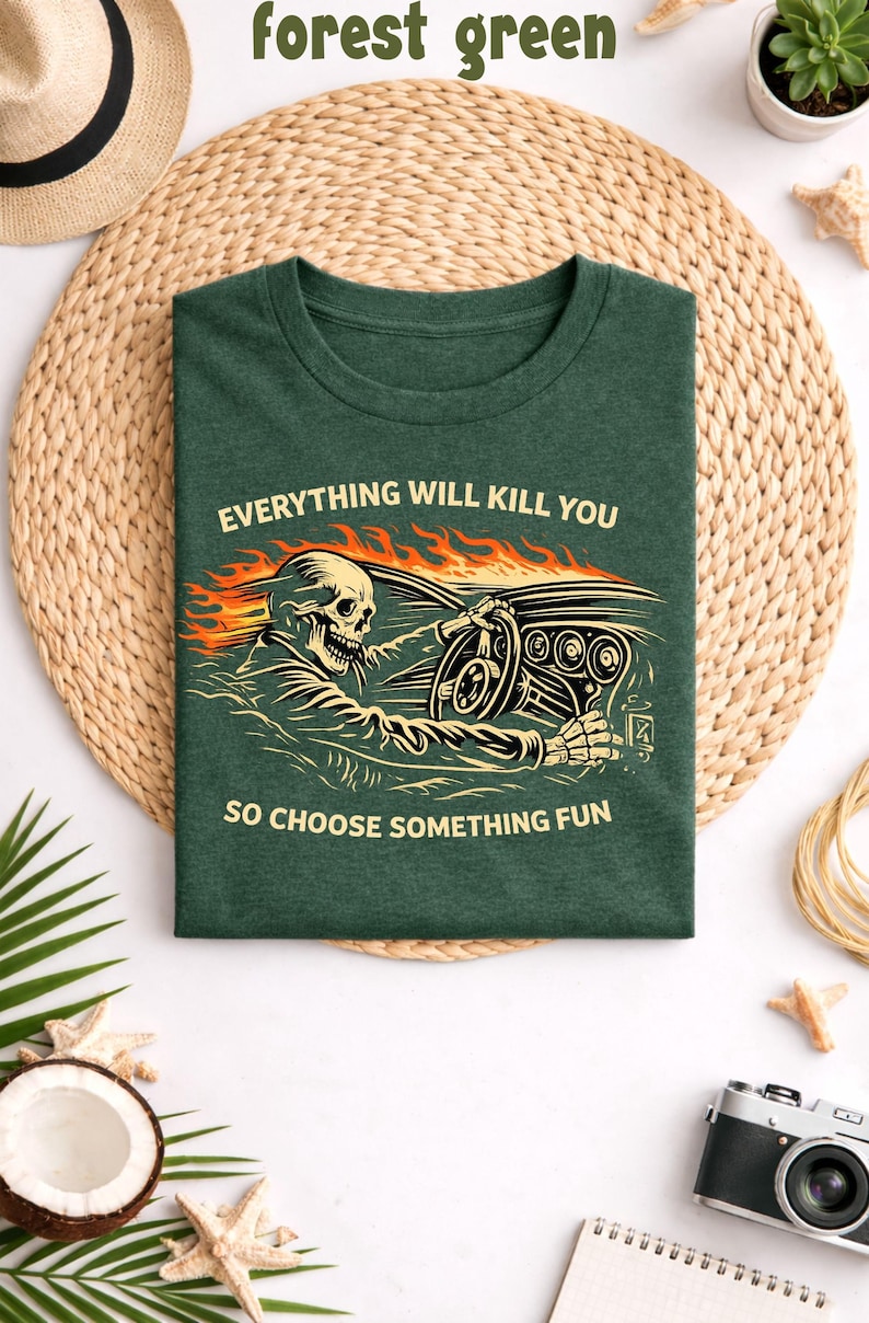displayed on a woven straw mat background with beach themed props including a straw hat, small plants, seashells, a notebook and a vintage camera. The shirt graphic shows a skeleton driving a classic car with flames flowing behind it. Above the illustration the phrase reads “EVERYTHING WILL KILL YOU” and below the image the text says “SO CHOOSE SOMETHING FUN.” The artwork uses a retro style color palette with orange flames, cream lettering, and a vintage line-art skeleton driver gripping a