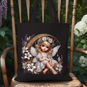 K&ouml;nnte beinhalten: Schwarze Tragetasche mit einer Illustration einer Fee. Die Fee mit blonden Haaren und wei&szlig;en Fl&uuml;geln sitzt in einem goldenen Halbmond, der mit wei&szlig;en Lilien und lila Lavendel geschm&uuml;ckt ist. Die Tasche hat schwarze Griffe.