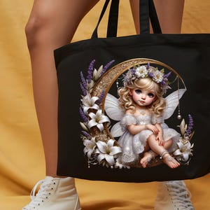 K&ouml;nnte beinhalten: Schwarze Tragetasche mit einer Fee-Illustration. Die Fee hat blondes Haar, wei&szlig;e Fl&uuml;gel und ein wei&szlig;es Kleid und sitzt auf einem Halbmond, umgeben von wei&szlig;en Lilien und lila Lavendel. Die Tasche hat schwarze Griffe.