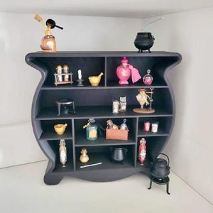 Könnte beinhalten: Ein schwarzes Regal mit dem Thema Tränke, gefüllt mit Miniatur-Apothekenartikeln. Die Regale beherbergen kleine Flaschen, Gläser, Mörser, Stößel und Kessel. Eine rosa Parfümflasche und ein kleiner schwarzer Kessel sind sichtbar.