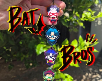 May include: A vertical acrylic keychain featuring four chibi-style superhero characters connected by black metal jump rings. The characters include figures in red, blue, purple, and green outfits. The text BAT BROS is displayed in bold red and black lettering.