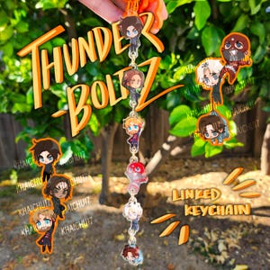Könnte beinhalten: Eine Kette mit Anhängern von Zeichentrickfiguren. Die Kette hat eine Reihe von kleinen, farbenfrohen Acryl-Anhängern. Die Wörter "THUNDERBOLTZ" und "LINKED KEYCHAIN" sind in Orange dargestellt.