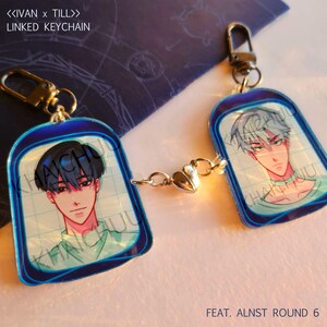Puede incluir: Llavero enlazado con dos retratos estilo anime, unidos por una cadena con un dije de coraz&oacute;n. Cada llavero tiene un borde azul y un cierre dorado. El texto "<<IVAN x TILL>> LINKED KEYCHAIN" es visible.