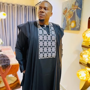 May include: A black traditional outfit featuring a decorative white and grey embroidered panel. The long-sleeved garment has a flowing design and is worn with a matching shawl. Suitable for special occasions.