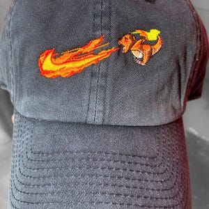 Peut inclure: Une casquette de baseball noire avec un motif brodé d'un personnage de dessin animé avec des flammes et un logo swoosh.
