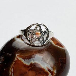 May include: A silver ring with a pentagram design. The ring is sitting on a brown and white agate stone.
