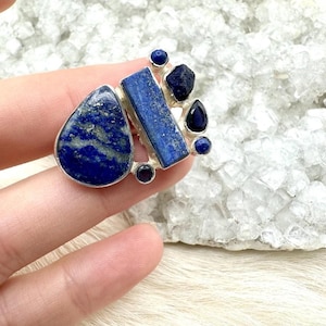 May include: A silver ring with a blue lapis lazuli stone set in a teardrop shape. The ring also features smaller blue lapis lazuli stones and a silver band.