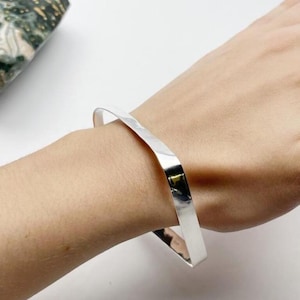 May include: A silver square bangle bracelet with a smooth, polished finish.