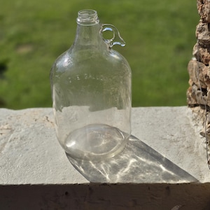 May include: A clear glass one-gallon jug with a handle. The jug is empty and has a textured surface.