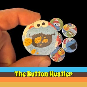 May include: A collection of colorful round buttons featuring Sesame Street characters, including Cookie Monster. The buttons are held in a hand against a black background. The text "The Button Hustler" is at the bottom.
