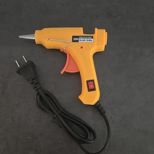 May include: A yellow electric glue gun with a black power cord. The glue gun has a red on/off switch and the text "CE GLUE GUN 20W 100-240V 50-60Hz" printed on the side.
