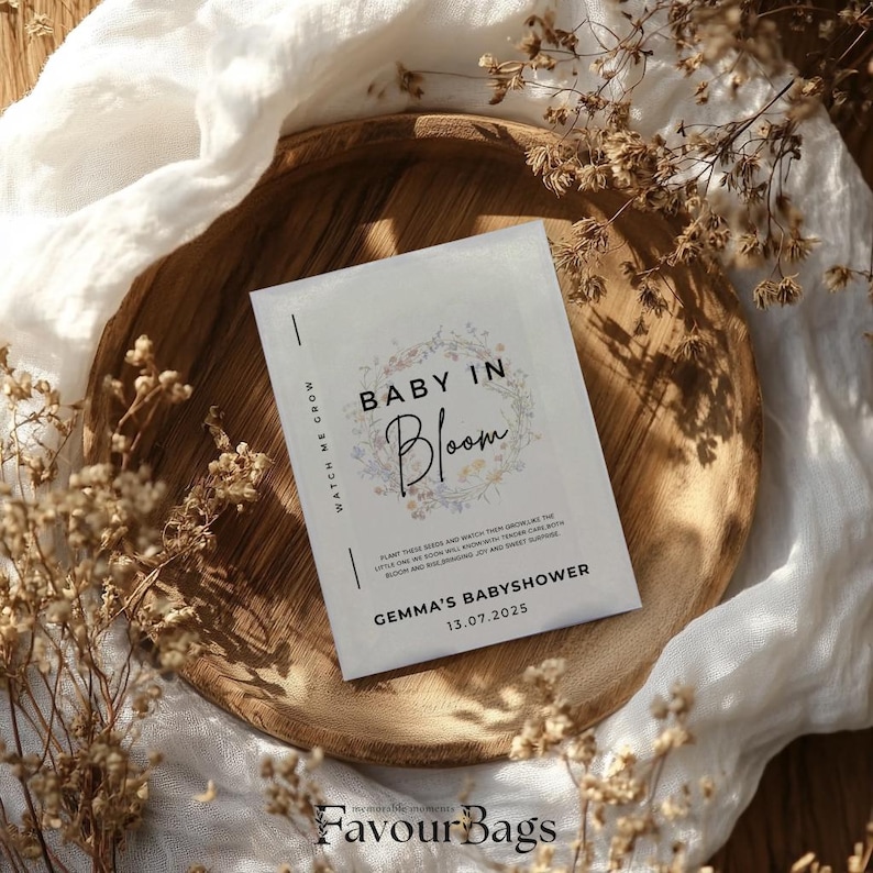 Pode incluir: Um cart&atilde;o branco com o texto "Baby in Bloom" em letras pretas com um design floral. O cart&atilde;o tamb&eacute;m inclui o texto "Gemma's Baby Shower" e a data "13.07.2025".