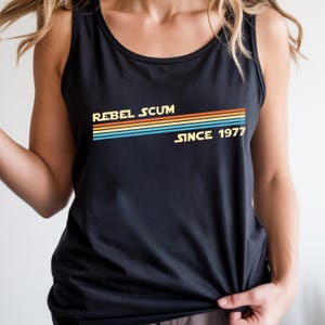 May include: Black tank top with the text "REBEL SCUM" above a retro-style stripe design in orange, yellow, blue, and teal, with "SINCE 1977" below. The top is sleeveless.