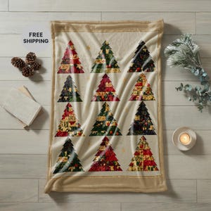 Peut inclure: Un plaid rectangulaire au fond crème orné d'un motif répétitif de douze sapins de Noël stylisés. Chaque sapin est composé de divers segments de style patchwork dans des tons de rouge, de vert et de doré disposés en grille.