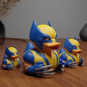 Pode incluir: Três patos de borracha amarelos e azuis em forma de Wolverine, um super-herói da Marvel Comics. Os patos têm garras e um traje amarelo e azul.