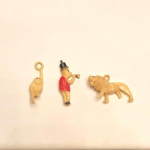 May include: Three small, vintage circus-themed figurines. Includes a monkey hanging from a ring, a man in a red coat playing a trumpet, and a lion. All are tan-colored plastic.