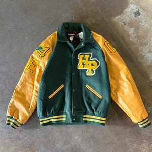 May include: A varsity jacket featuring a dark green wool body and yellow leather sleeves. The front displays a yellow and white embroidered HP patch. The sleeves have yellow and green striped ribbed cuffs and a yellow patch with the number 94.