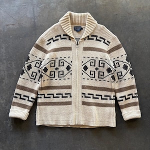 Può includere: Un cardigan beige con zip e motivo geometrico marrone e nero. Il cardigan ha un collo a scialle e polsini a coste. Il design include forme a diamante e rettangolari. Lavorato a maglia.