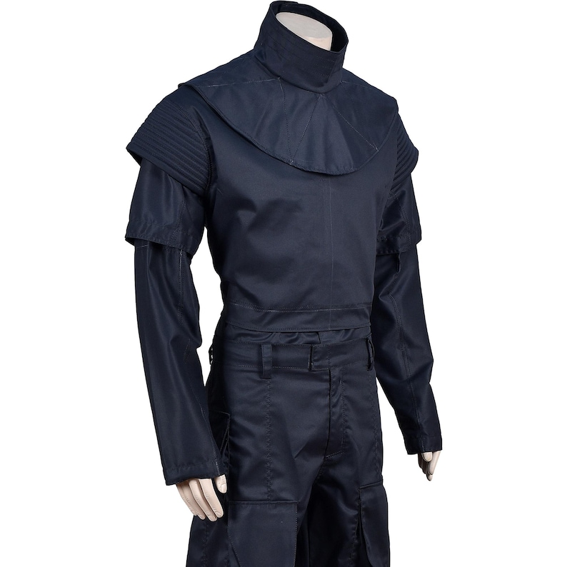 Puede incluir: Un mono azul oscuro con cuello alto y mangas largas. El mono tiene un cintur&oacute;n y bolsillos.