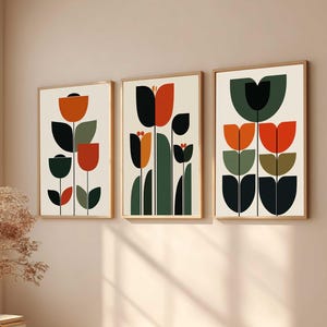Può includere: Tre stampe artistiche incorniciate con disegni floreali astratti. Ogni stampa presenta una disposizione unica di forme geometriche in arancione, nero, verde e crema. Le opere d'arte sono esposte in una stanza ben illuminata, suggerendo un design d'interni moderno.