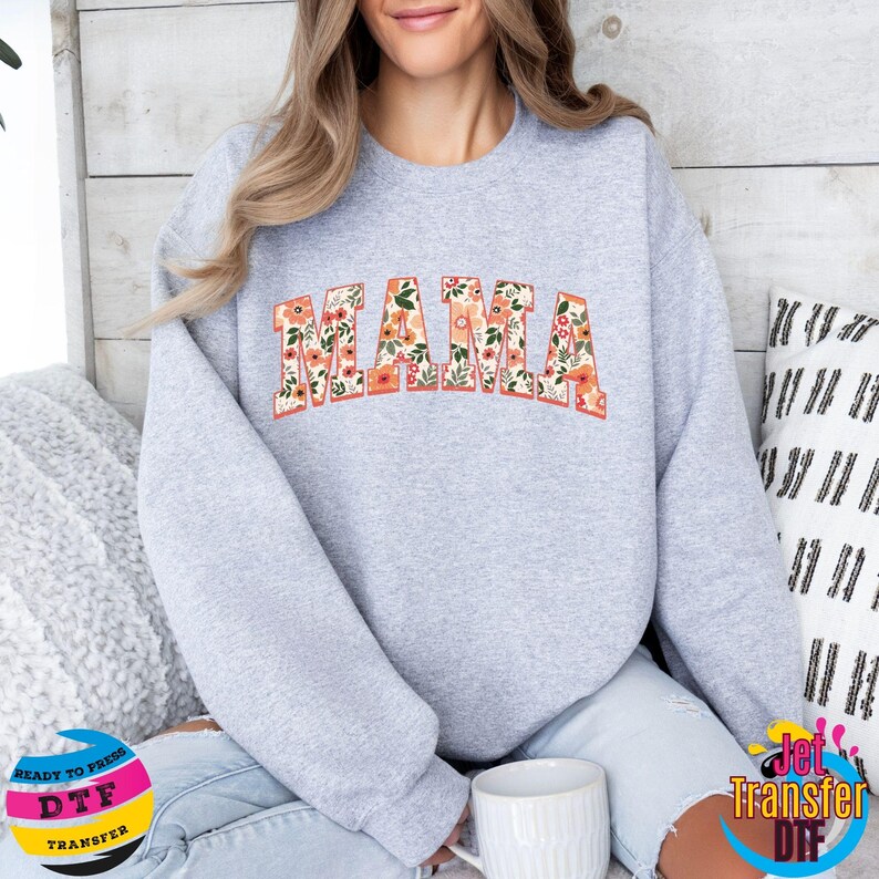 May include: Gray sweatshirt with the word "MAMA" in floral print letters. The sweatshirt is a crew neck style with long sleeves.