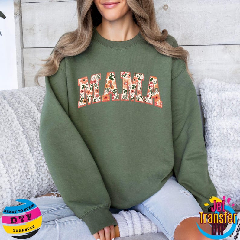 May include: A green sweatshirt with the word "MAMA" in floral print letters. The sweatshirt is a crew neck style with long sleeves.