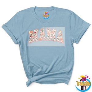 May include: A light blue t-shirt with a floral design that says "MAMA" in a bold, white font.