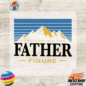 May include: A white transfer sheet with a mountain and sky design. The text reads "IT'S NOT A DAD BOD IT'S A FATHER FIGURE". The design includes blue horizontal lines, yellow mountains, and black text.