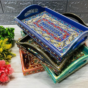 May include: A set of four intricately painted wooden trays with decorative floral patterns. The trays are stacked on top of each other, with the top tray being blue, the second black, the third red, and the bottom green.
