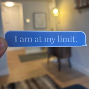May include: A blue sticker in the shape of a text message bubble with the words "I am at my limit" in white text. The sticker is held in front of a blurred background.