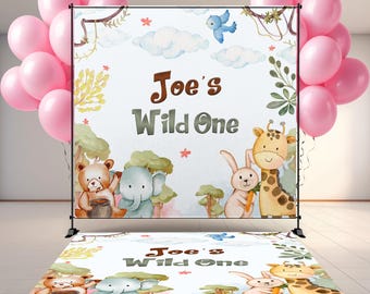 May include: A backdrop and floor decal set with a jungle theme. The backdrop features the text "Joe's Wild One" with illustrations of a bear, elephant, rabbit, and giraffe. Pink balloons are on either side of the backdrop.