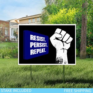 May include: A white sign with the words "RESIST. PERSIST. REPEAT." in white text on a blue background, and a white fist on a black background. The sign is displayed on a green lawn.
