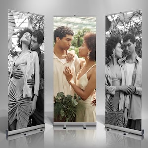 May include: Three vertical roll-up banners featuring couples in various poses. The banners display black and white photographs of a man and woman embracing. The banners have a silver base and a retractable mechanism.