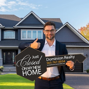 May include: A man in a suit holds a large key-shaped sign that reads "Just Closed On My New Home" and "Dominion Realty". The man is smiling and giving a thumbs up in front of a house.
