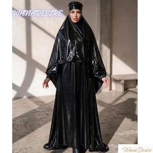 Peut inclure: Image d'une personne portant une tenue noire brillante avec une capuche et une longue robe. La tenue comprend un haut en forme de cape. Le texte "WANADESTRE" est visible en haut à gauche, et "Wana Desire" en bas à droite.