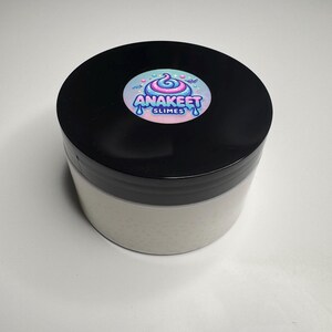 Pode incluir: Um recipiente de slime branco com uma tampa preta. A tampa tem um adesivo colorido com o texto "Anakeet Slimes".