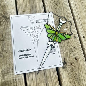 Może przedstawiać: Witrazowy sztylet Luna Moth z zielono-żółtym motylem, zawieszony na łańcuchu. Obok znajduje się kartka z wzorem i tekstem "@KOZLOOPERGLASS Luna Moth Dagger Stained Glass Pattern".