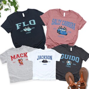 Pode incluir: Cinco camisetas de manga curta em v&aacute;rias cores, cada uma com um nome diferente e um gr&aacute;fico de carro de desenho animado. As camisas incluem os nomes "FLO", "SALLY CARRERA", "MACK", "JACKSON" e "GUIDO", com "CARS" e o ano "2006" tamb&eacute;m impressos.