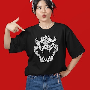 May include: Black t-shirt featuring a white graphic of a Bowser-like character composed of various cartoon figures. The shirt has short sleeves and a crew neck. The person in the image is wearing blue jeans and a white bandana.