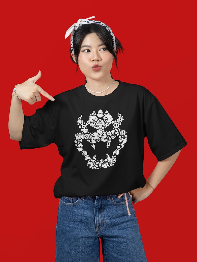 May include: Black t-shirt featuring a white graphic of a Bowser-like character composed of various cartoon figures. The shirt has short sleeves and a crew neck. The person in the image is wearing blue jeans and a white bandana.