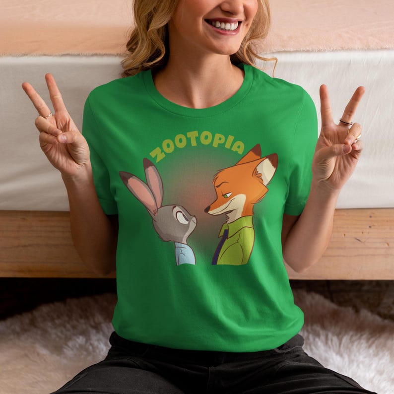 May include: Green t-shirt featuring a graphic of Judy Hopps and Nick Wilde from the film Zootopia. The text "Zootopia" is printed in a yellow and orange gradient.