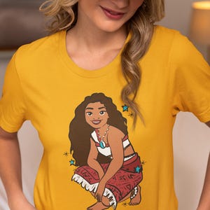 May include: A yellow t-shirt with a cartoon image of Moana from the Disney movie Moana. Moana is wearing a red and white outfit and is sitting in a crouched position. The image is surrounded by blue stars.