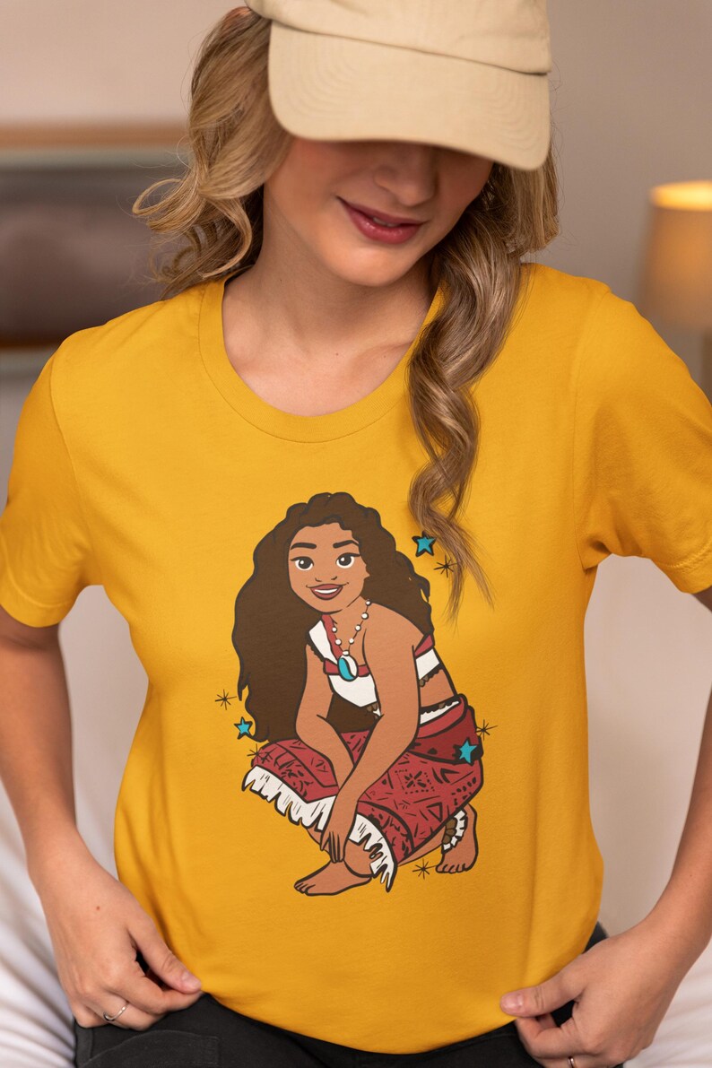 May include: A yellow t-shirt with a cartoon image of Moana from the Disney movie Moana. Moana is wearing a red and white outfit and is sitting in a crouched position. The image is surrounded by blue stars.