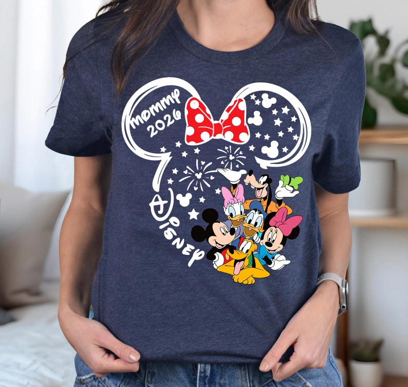 Puede incluir: Camiseta azul marino con un dise&ntilde;o de orejas de Mickey Mouse blancas y un lazo rojo de lunares. El dise&ntilde;o incluye el texto "mommy 2026" y los personajes de Disney Mickey, Minnie, Donald, Daisy, Goofy y Pluto.