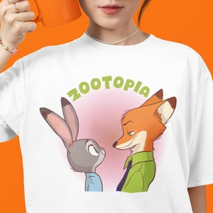 May include: White t-shirt featuring a graphic of Judy Hopps and Nick Wilde from the film Zootopia. The text "Zootopia" is written in green above the characters.