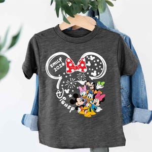 Puede incluir: Camiseta gris oscuro con un dise&ntilde;o de Disney. El dise&ntilde;o incluye orejas de Mickey Mouse con un lazo rojo, el nombre "Emily 2020" y varios personajes de Disney. Tambi&eacute;n se incluye la palabra "Disney".