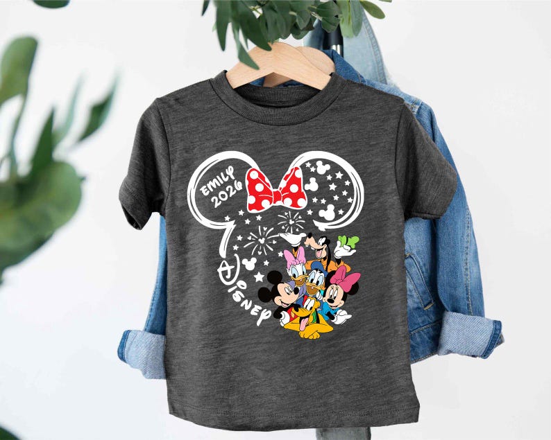 Puede incluir: Camiseta gris oscuro con un dise&ntilde;o de Disney. El dise&ntilde;o incluye orejas de Mickey Mouse con un lazo rojo, el nombre "Emily 2020" y varios personajes de Disney. Tambi&eacute;n se incluye la palabra "Disney".