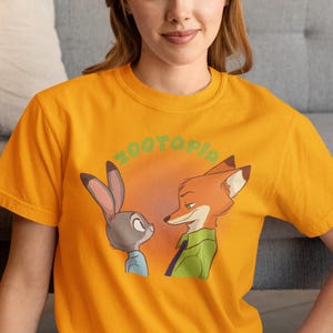 May include: A yellow t-shirt featuring a graphic of Judy Hopps and Nick Wilde from the film Zootopia. The text "Zootopia" is printed in green above the characters.